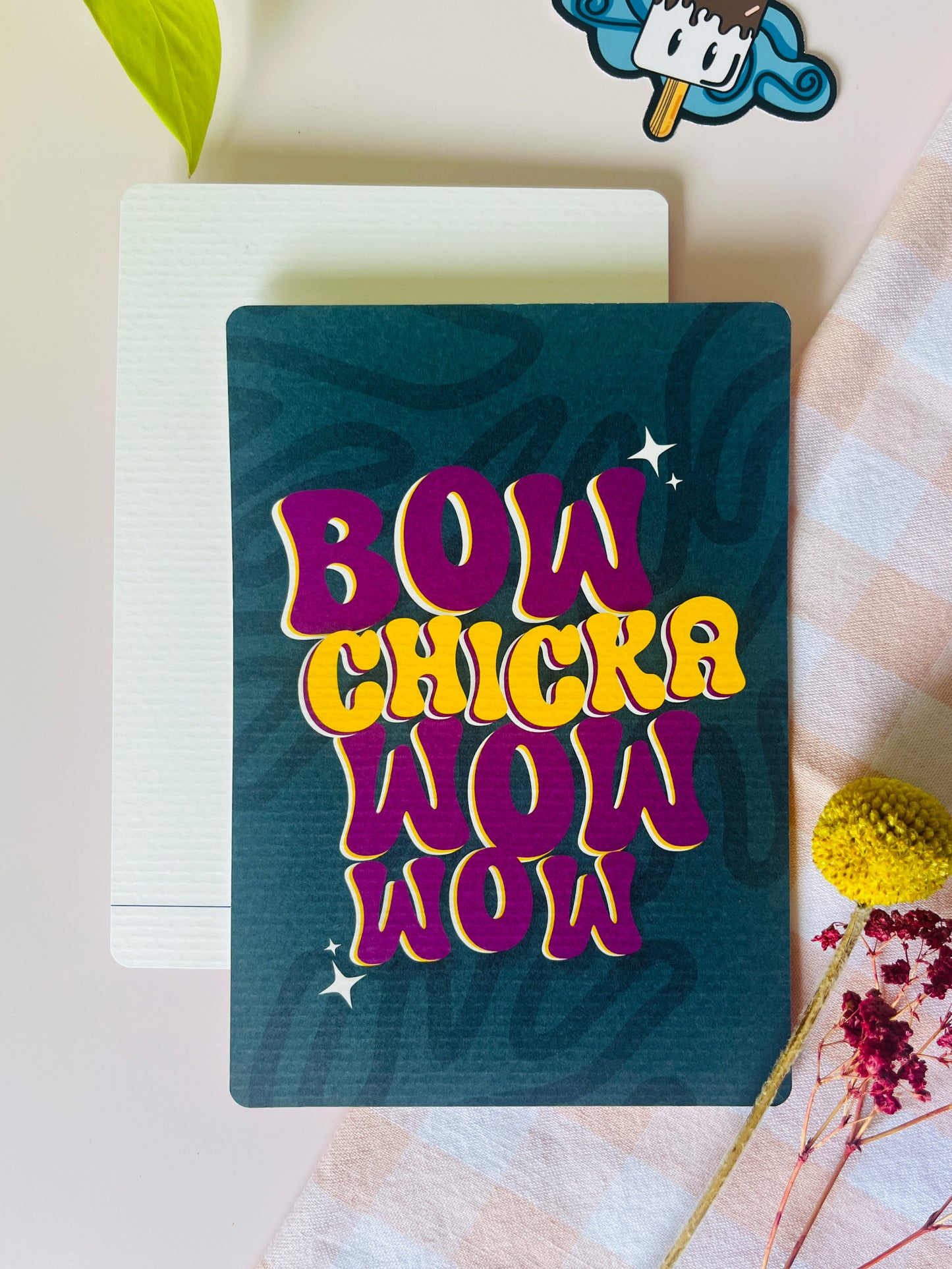 Ansichtkaart met groenige achtergrond met een flowey streeppatroon en de tekst bow chicka wow wow in roze/paars en geel. Ontwerp door Studio Dwarsdenker