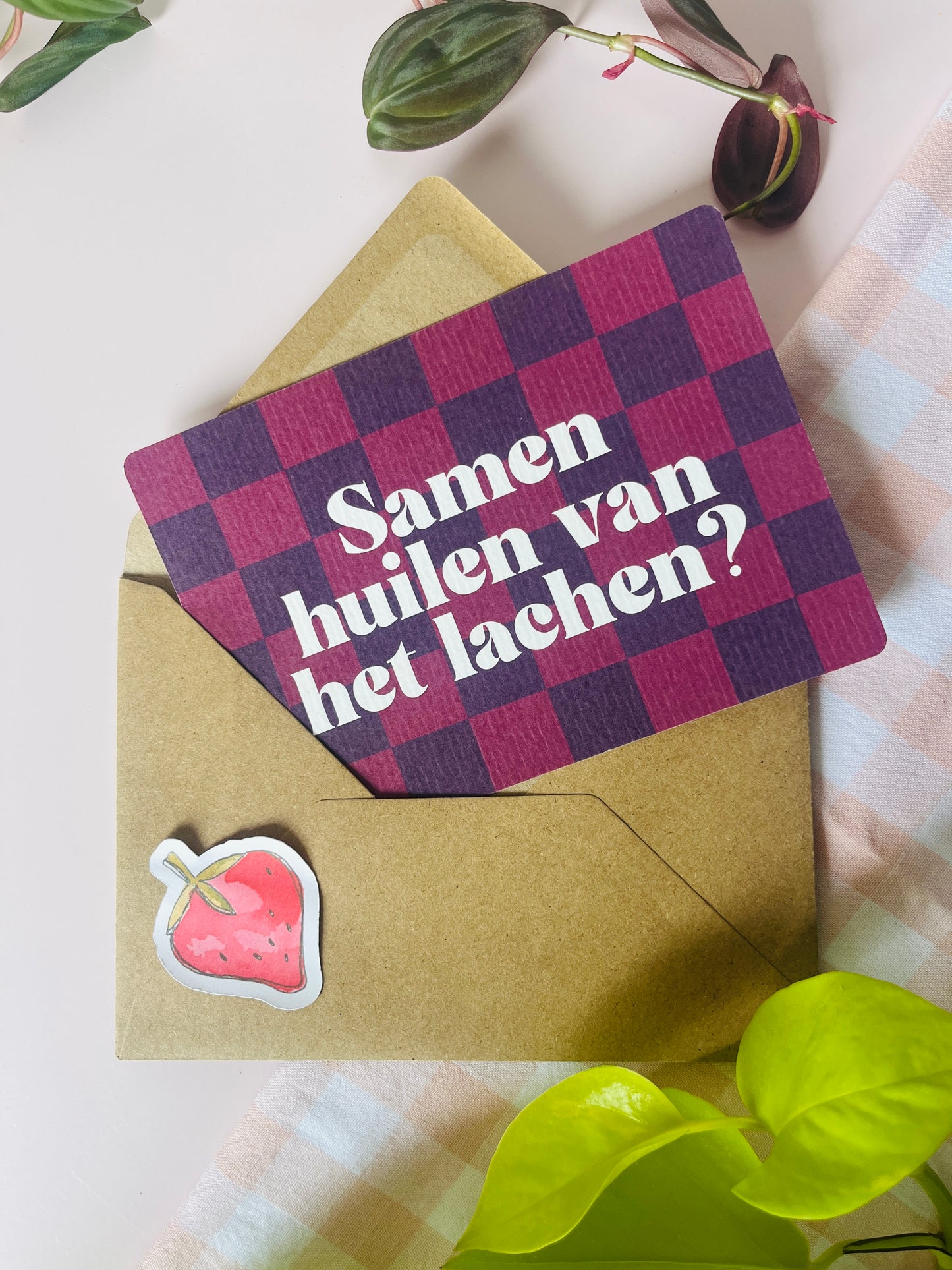 Ansichtkaart in roze paars tinten met een ruitenpatroon en de tekst: Samen huilen van het lachen. Ontwerp door Studio Dwarsdenker