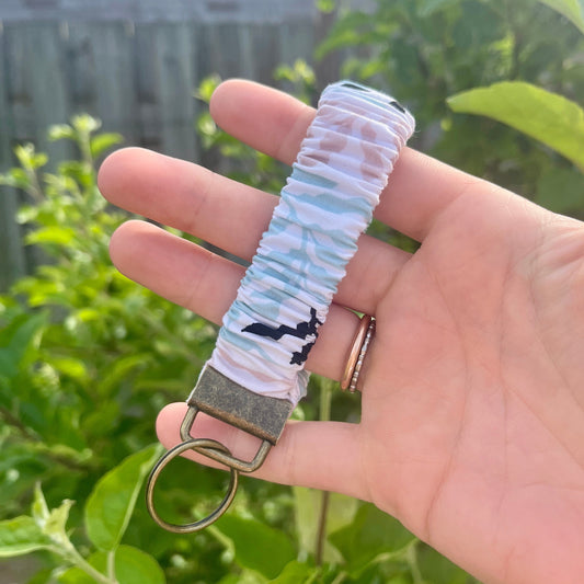 Sleutelhanger in de vorm van een  Scrunchie voor om je pols. Met stoffen bladeren patroon.= in pastel roze, blauw en zwart. Met bronskleurige klem/ring. Handgemaakt door Studio Dwarsdenker.