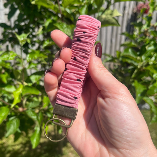 Sleutelhanger in de vorm van een  Scrunchie voor om je pols. Van stof met elastiek. Oud roze met kleine zwarte hartjes. Met bronskleurige klem/ring. Handgemaakt door Studio Dwarsdenker.