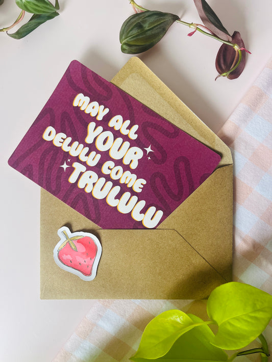 Ansichtkaart in roze paars tint met een gestreept partoon en de tekst may all your delulu come trululu. Ontwerp door Studio Dwarsdenker